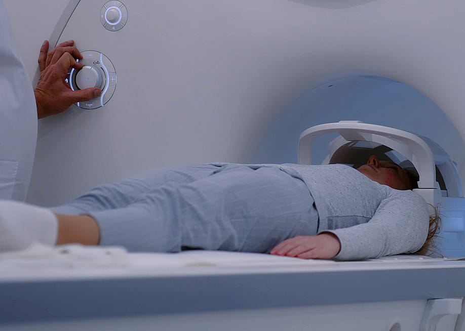 A female patient lies down on an MRI or CT scan bed moving inside the machine for scanning the brain and body. — Frame Stock Footage // Shutterstock