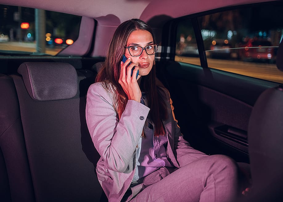 A young businesswoman in the backseat of a car late at night and talking on the phone. — Zamrznuti tonovi // Shutterstock