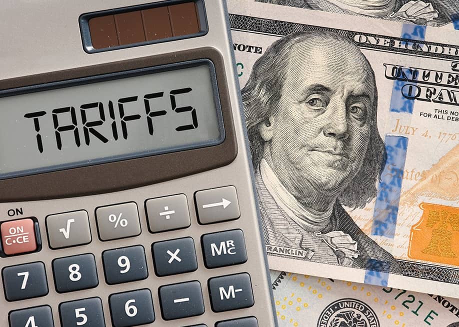 A calculator displaying the word 'tariffs' on top of a US dollar banknote. — Cagkan Sayin // Shutterstock