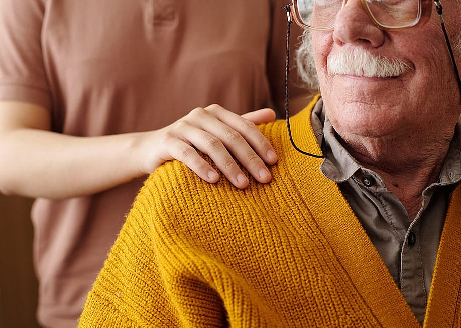 A young adult patting the shoulder of an elderly person as care and support. — Pressmaster // Shutterstock