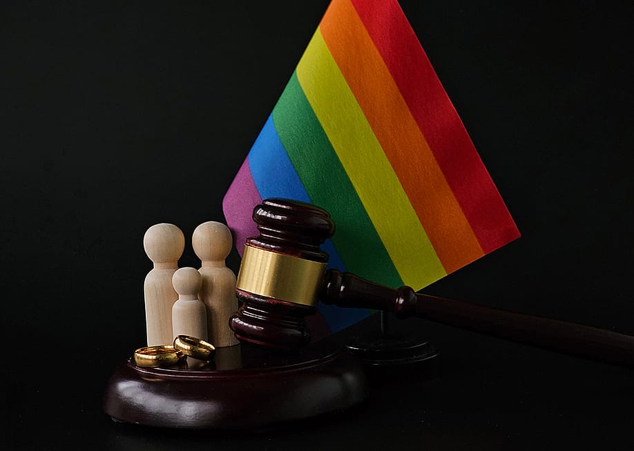 An LGBTQ+ rainbow flag with a figure of a family and judge's gavel as a concept of same-sex divorce. — NMK-Studio // Shutterstock
