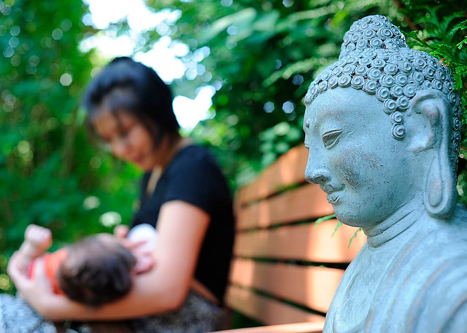 A Buddhist mother carrying and feeding her child outside in a park. — Godong // Universal Images Group via Getty Images