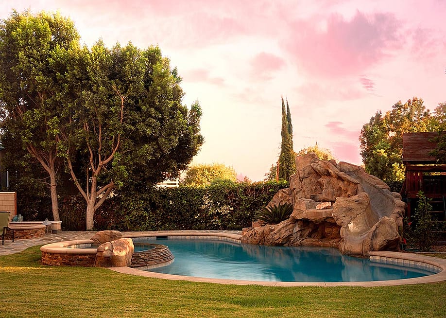 A modern backyard pool with rock waterfalls and slide. — Jahn Martin // Shutterstock
