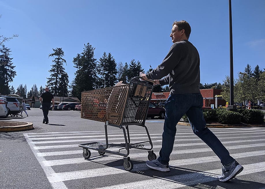 Street view of a man leaving with a supermarket with a grocery cart. — Colleen Michaels // Shutterstock