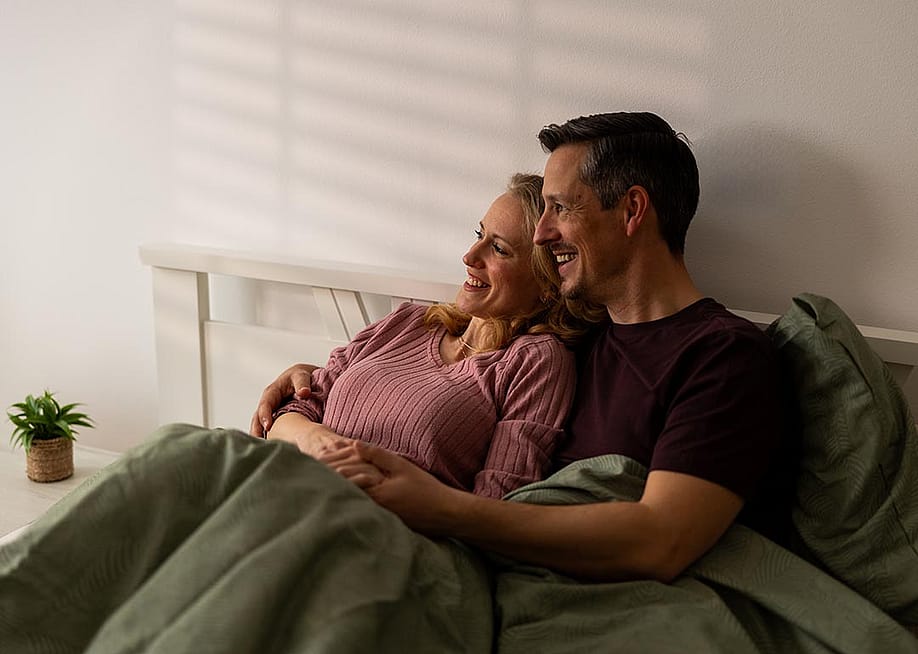 A couple sitting in bed wrapped in blankets. — MilanMarkovic78 // Shutterstock