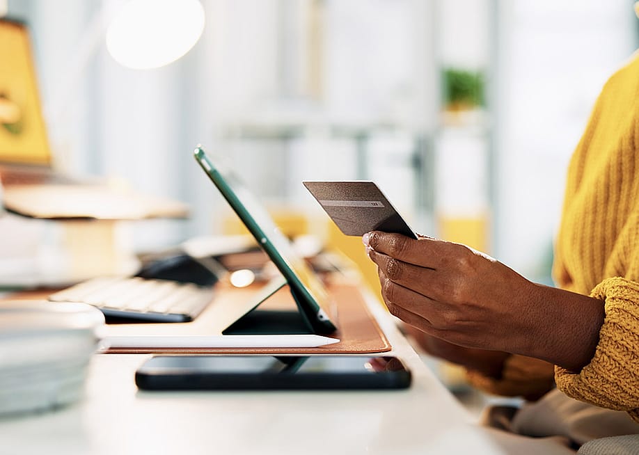 A business manager holding a credit card while checking digital transactions from a tablet. — PeopleImages // Shutterstock