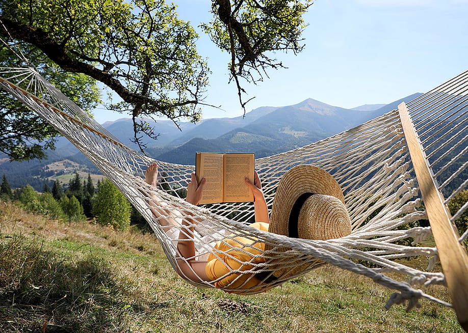 A person reading a book while relaxing in a hammock outdoors. — New Africa // Shutterstock