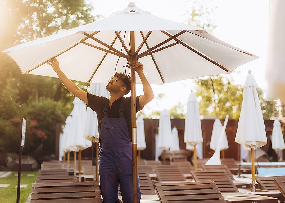 A hotel officer setting up a parasol beside the hotel's pool before guests' arrival. — Roman Fenton // Shutterstock