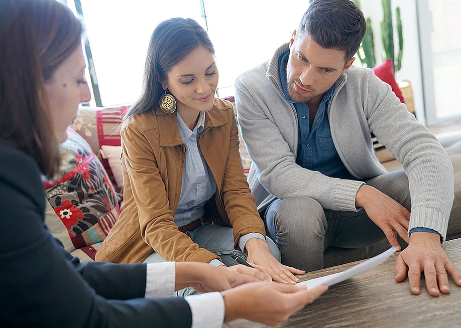 A couple reviewing a home investment contract with supervision from a financial advisor. — goodluz // Shutterstock