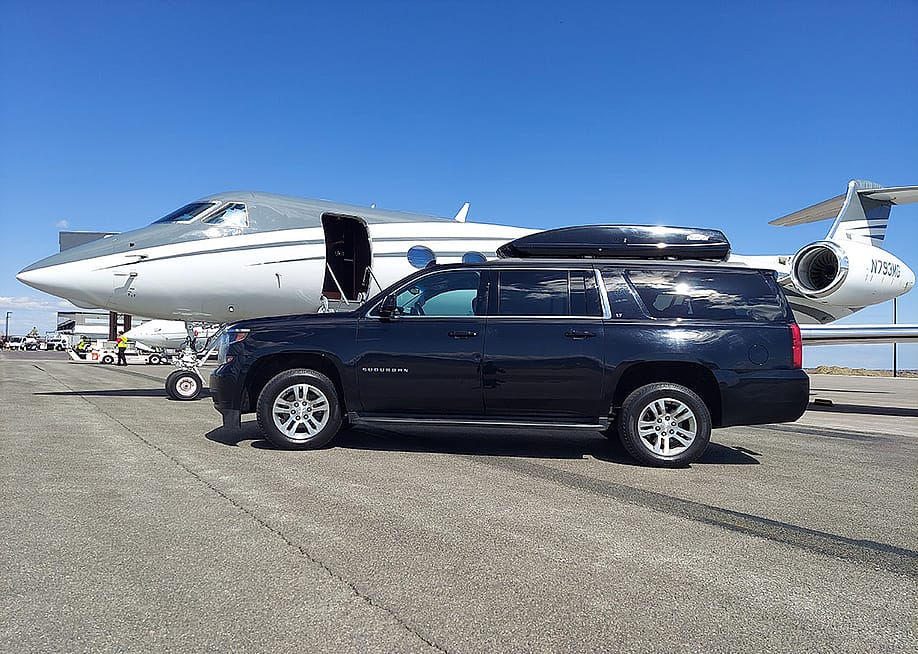 A black Chevrolet Suburban car parked alongside a private air jet in an open ground. — photo-denver // Shutterstock