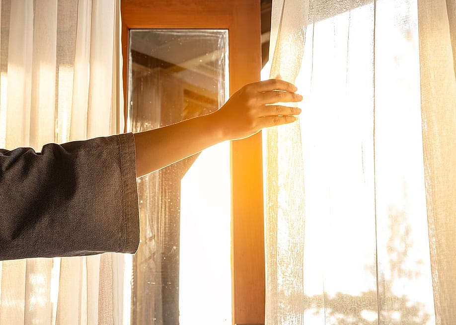 A woman's hand opening the curtains to a window to let in sunlight. — Me dia // Shutterstock