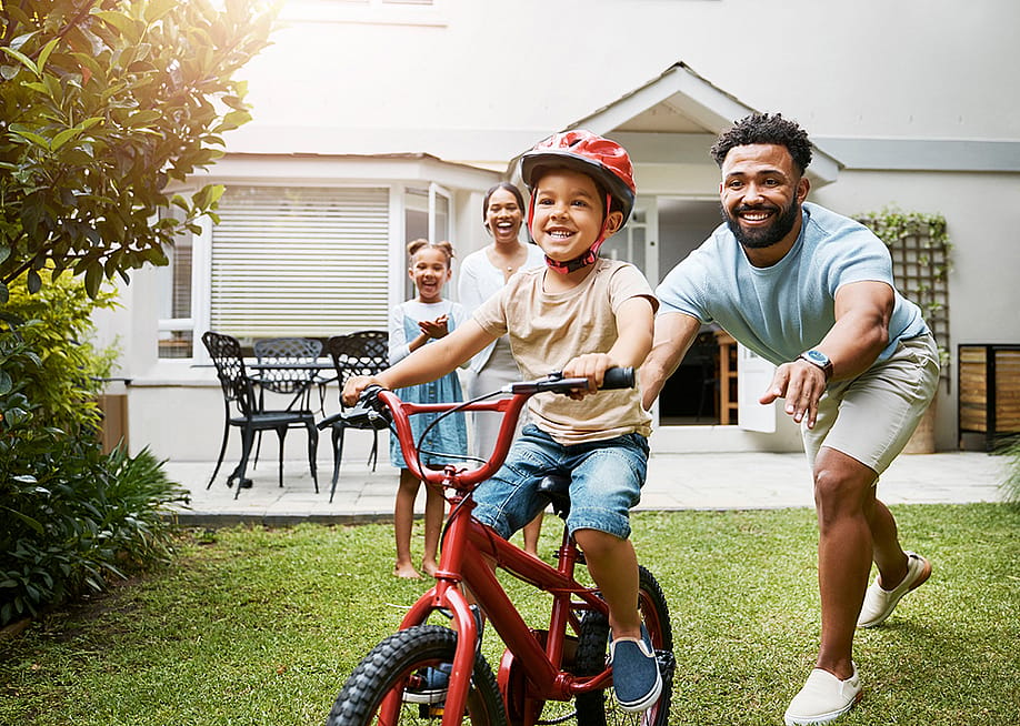 A young boy learning how to ride a bicycle being cheered on by his family. — PeopleImages // Shutterstock