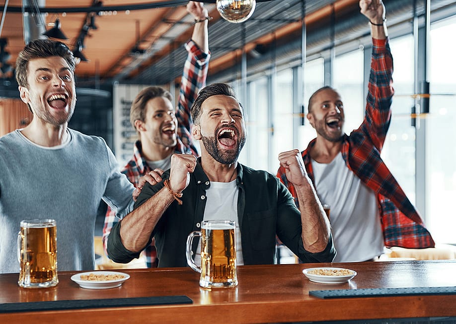 A group of men cheering and drinking beer while watching a sports game. — G-Stock Studio // Shutterstock