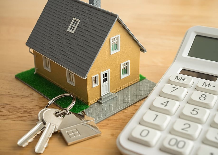 A small house model, house keys, and a white calculator as a concept of calculating rent. — Pla2na // Shutterstock
