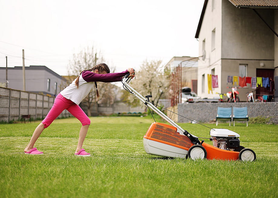 A teenager pushing an electric lawnmower in their backyard during a summer holiday. — Andrii Medvediuk // Shutterstock