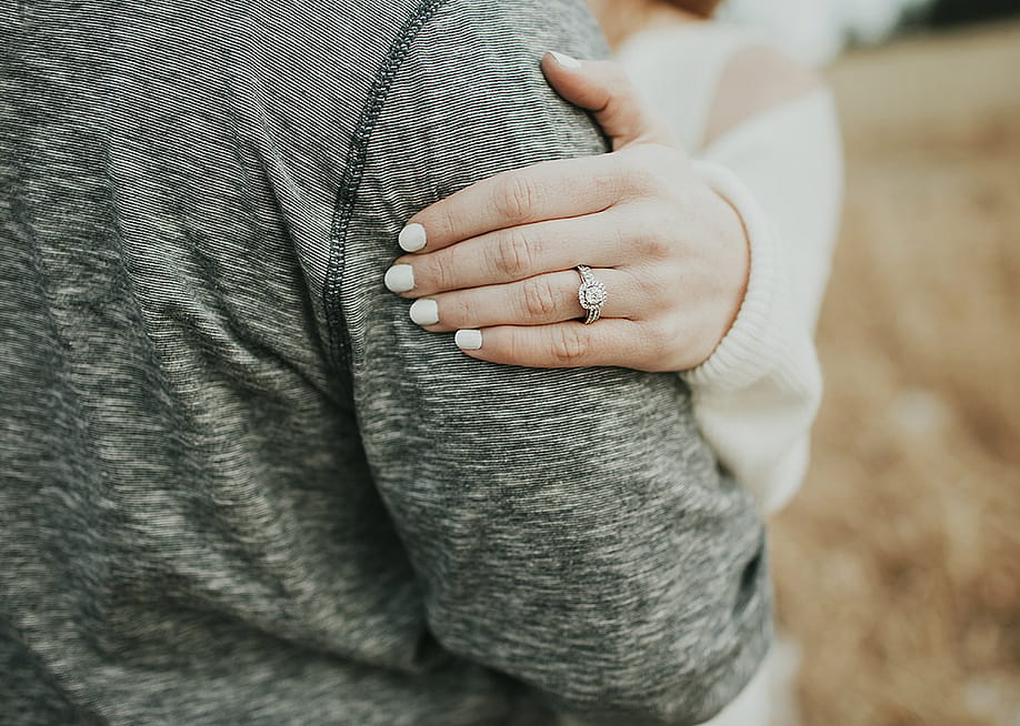 A diamond engagement ring on a woman's hand resting on her fiancé's arm. — Jenaphotography // Shutterstock