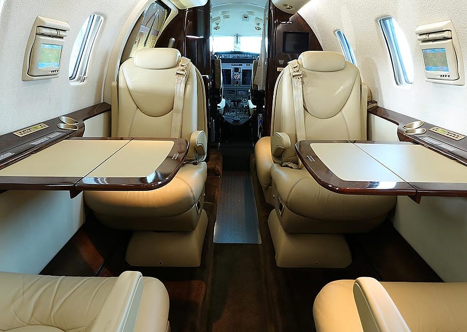 A private business jet cabin with open tables on both sides and lowered armrests. — O.Schaumann // Shutterstock