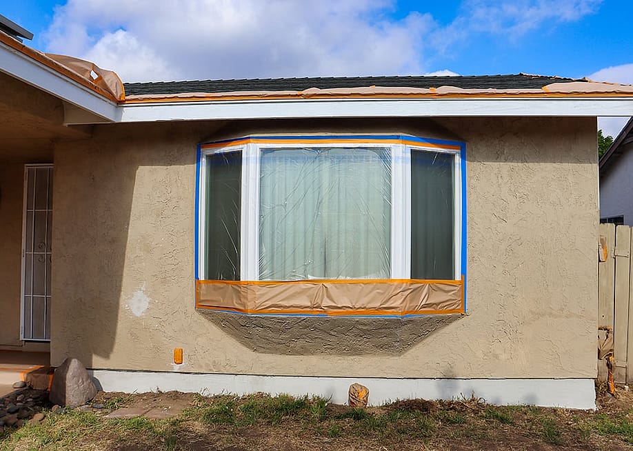 A portion of a house for sale covered with protective plastic for a repainting job. — Rosamar // Shutterstock