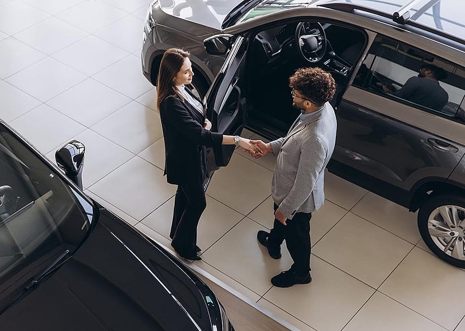 A car sales agent and a customer shaking hands after closing a deal in a car dealership shop. — Anatoliy Cherkas // Shutterstock