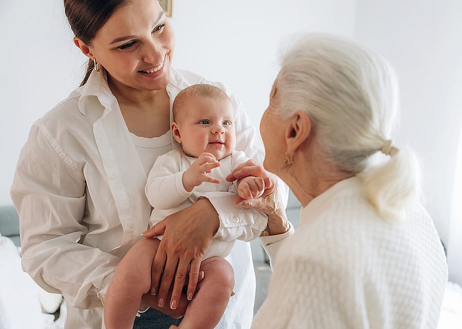 A grandmother looking at her adult daughter and newborn granddaughter. — Standret // Shutterstock