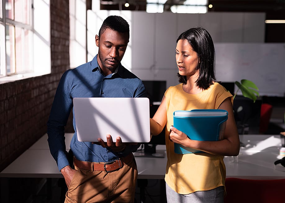 Two colleagues standing in an office discussing a task together. — wavebreakmedia // Shutterstock