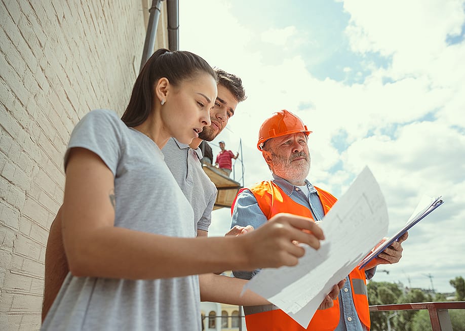 A foreman showing a young couple the plans to their new home. — Master1305 // Shutterstock