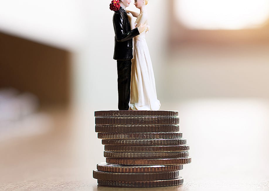 Figure of a married couple on top of a stack of coins as a concept of saving for a wedding. — Monster Ztudio // Shutterstock
