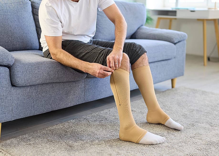 A man putting on knee-high compression stockings at home. — Studio Romantic // Shutterstock