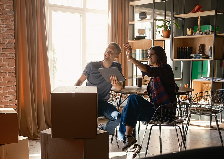 A couple surrounded with packed boxes discussing room organization after moving in. — Arthur Bargan // Shutterstock