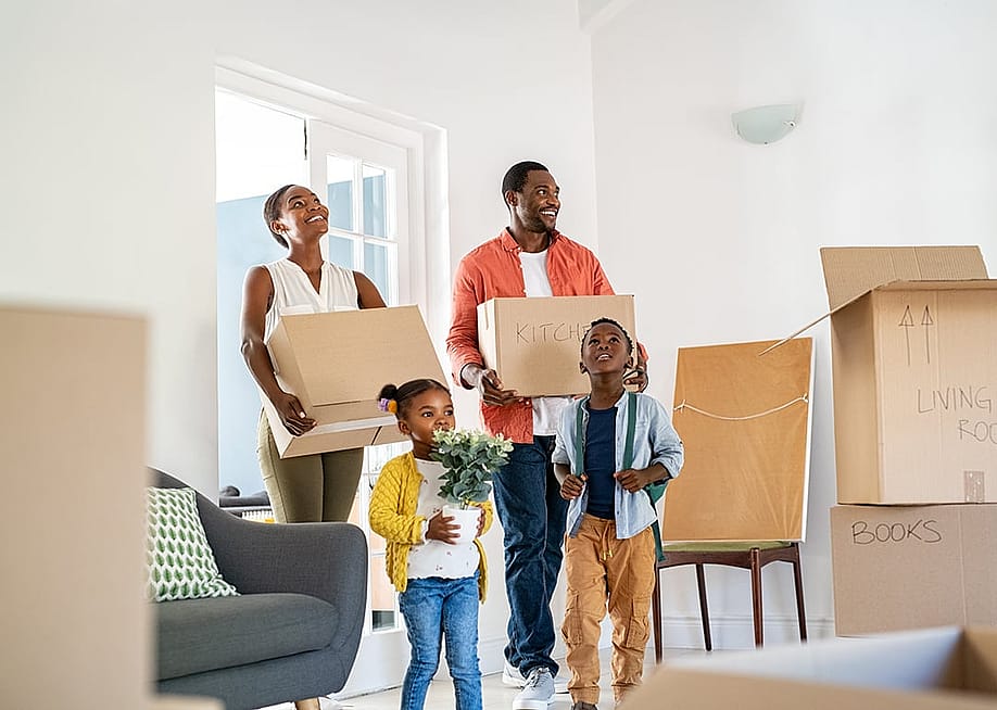 A happy family of four moving into their new home, surrounded by cardboard boxes labeled for different rooms. — Ground Picture // Shutterstock