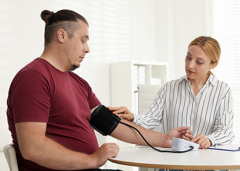 A nutritionist measuring a patient's blood pressure using a manual sphygmomanometer in a clinic. — New Africa // Shutterstock
