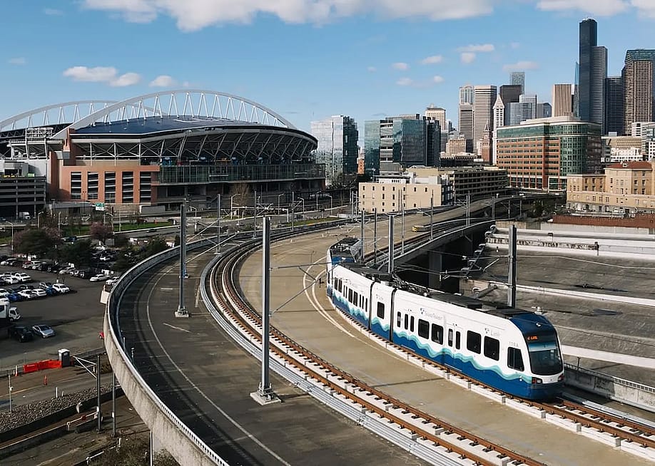 A Sound Transit Link light rail train, with the Lumen field and Seattle skyline in Washington, USA. — Courtesy of Sound Transit