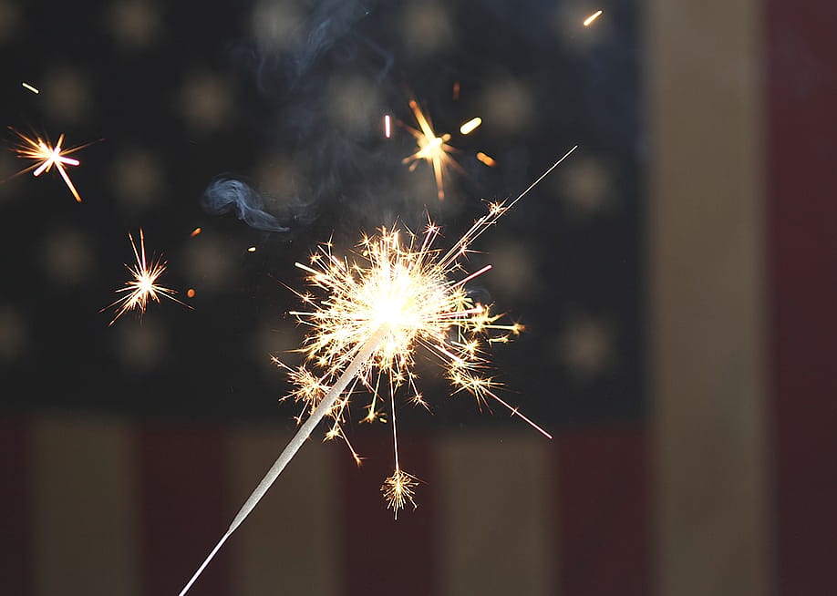 A sparkler firework with the US flag in the background for the 4th of July celebrations. — iHumnoi // Shutterstock