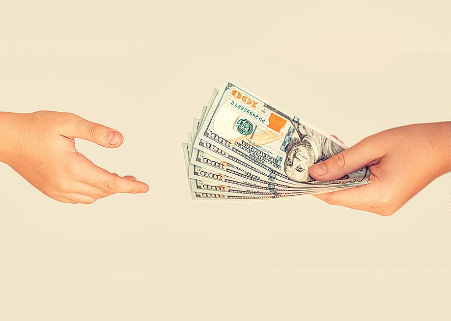 A financial transaction where one person is handing US banknotes to another person. — Body Stock // Shutterstock