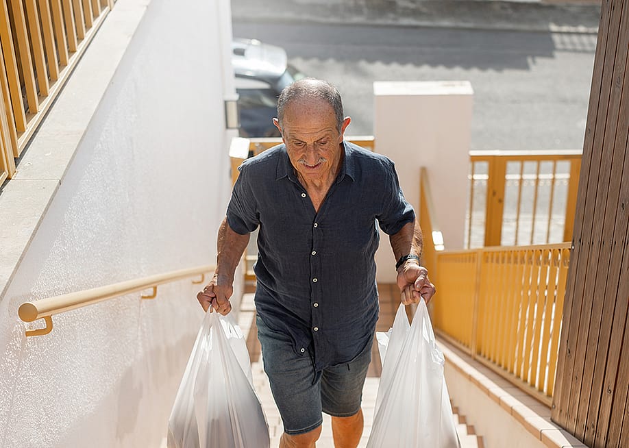 An elderly person walking up the stairs while carrying grocery bags. — Basilico Studio Stock // Shutterstock