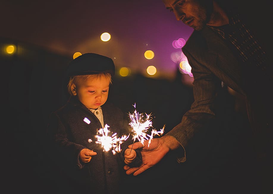 A father helping his young child with sparklers during a New Year celebration. — Tomsickova Tatyana // Shutterstock