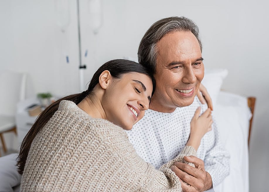A daughter hugging her father, who is recovering from an illness in the hospital. — LightField Studios // Shutterstock