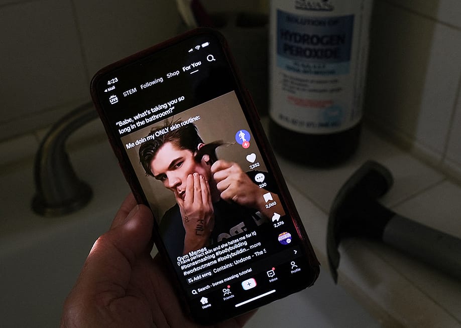 A person watching from his smartphone a video of a male TikTok influencer hammering his cheekbone, while a hydrogen peroxide bottle and a hammer are also seen in his bathroom. — CHRIS DELMAS // AFP via Getty Images