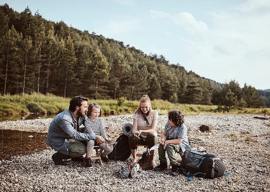 A family camping beside a small creek and cooking fish over a campfire. — Geber86 // Shutterstock
