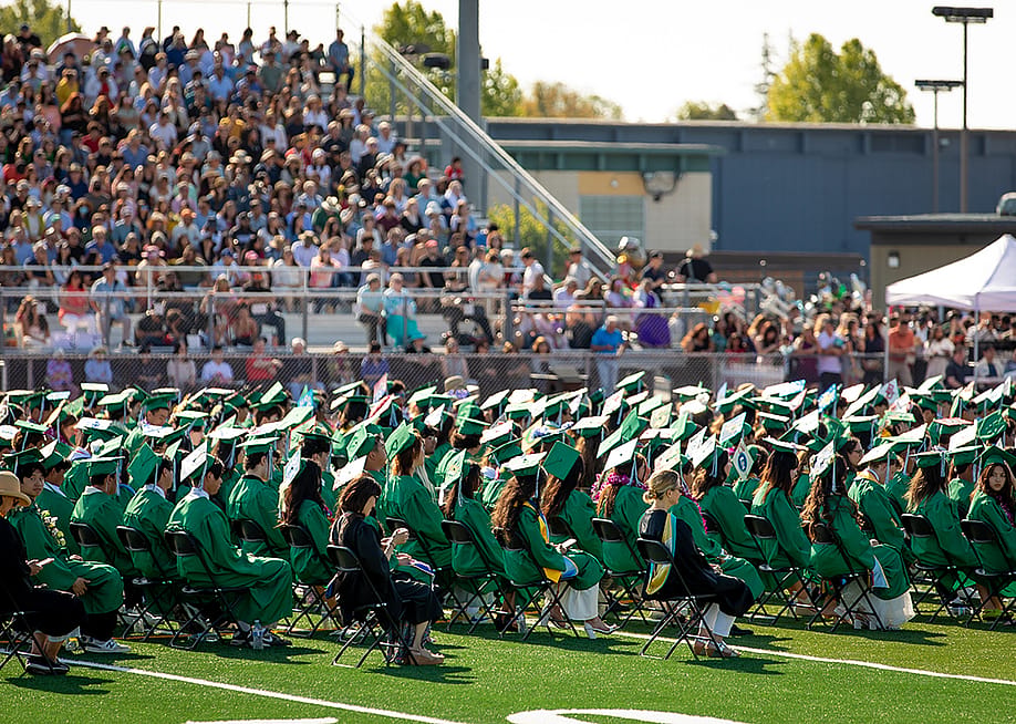 A high school graduation ceremony happening outdoors in the campus' sports field. — bluestork // Shutterstock