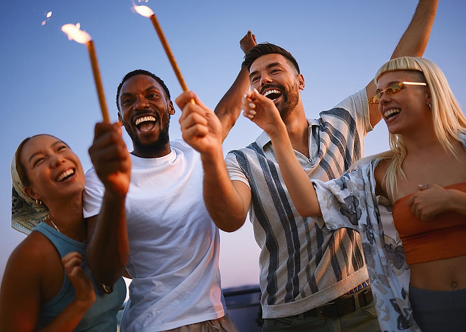A group of friends celebrating together with sparklers during a rooftop party at sunset. — djile // Shutterstock