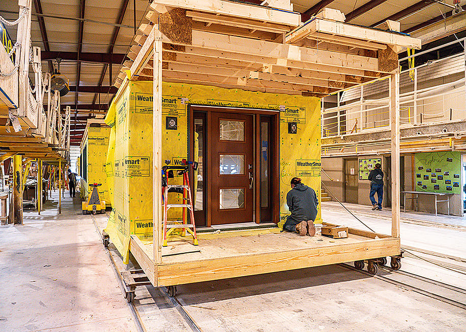 A worker kneels on a wooden platform building a modular home under construction in a factory in Middleburg, Pennsylvania. — Courtesy of Apex Homes and the Modular Home Builders Association