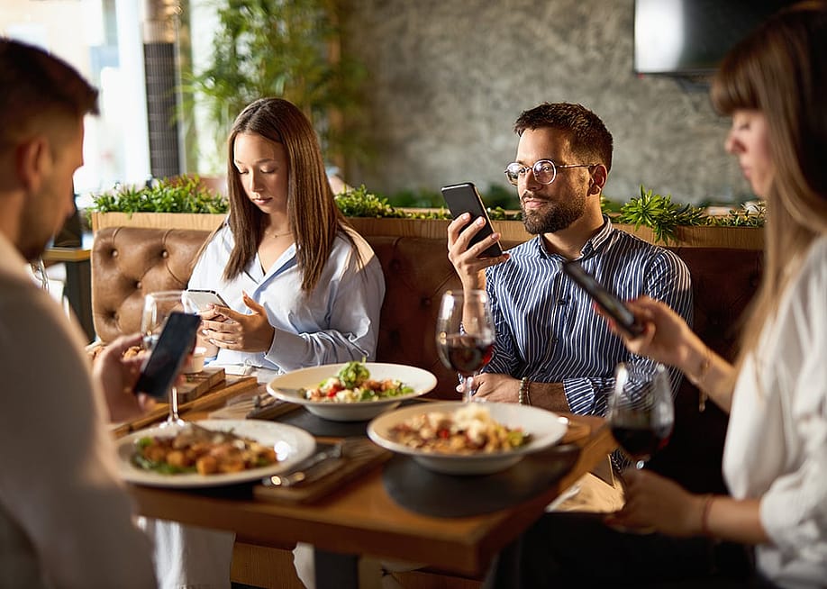 A group of business colleagues checking their smartphones while eating lunch in a restaurant. — Goksi // Shutterstock