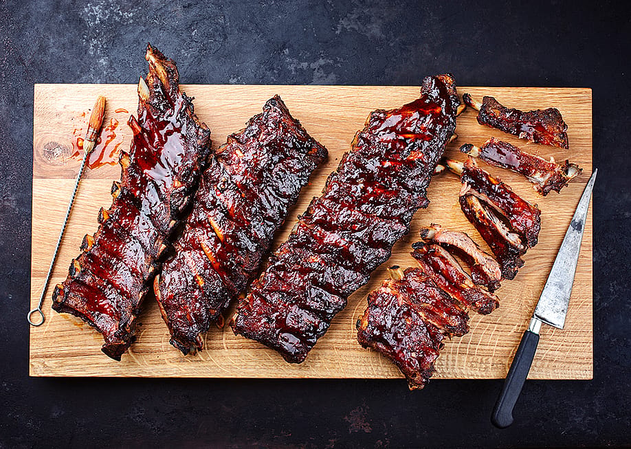 Slabs of freshly barbecued ribs sliced on a wooden cutting board. — hlphoto // Shutterstock