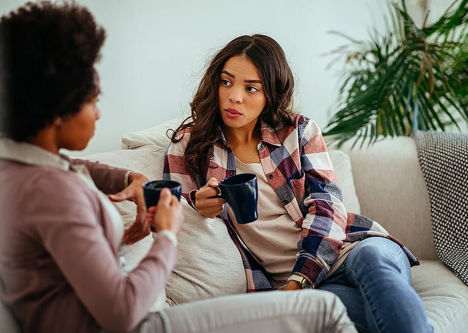 Two female friends having a discussion at home while drinking coffee. — bbernard // Shutterstock