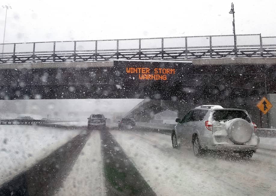 Windshield POV of a car passing under a bridge with an electronic 'Winter Storm Warning' sign. — Upstate Photos // Shutterstock