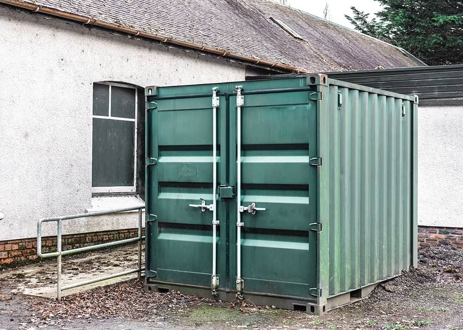 A large steel storage container positioned outdoors beside a building. — Antoni M Lubek // Shutterstock