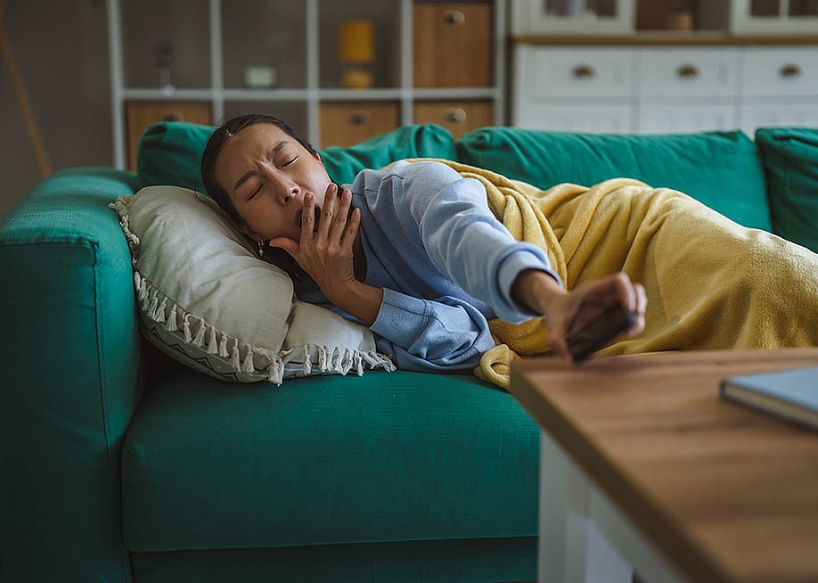 A young woman at home yawning and lying comfortably on a green couch. — Miljan Zivkovic // Shutterstoc