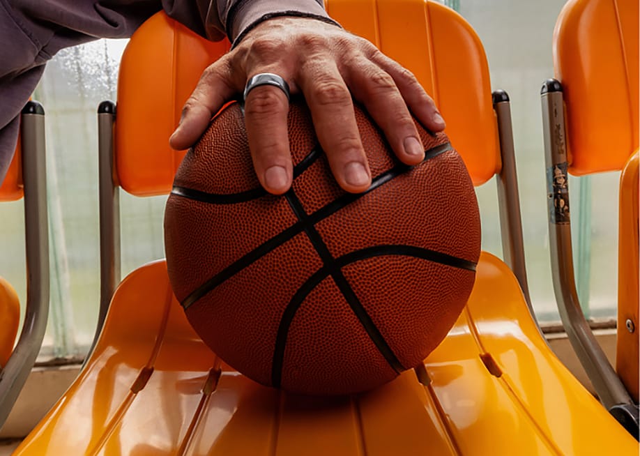 A player's hand wearing an Oura ring placed over a basketball. — Oura