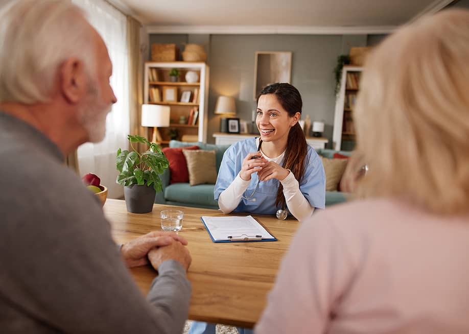 A nurse discussing health issues and plans to elderly patients during a home visit. — StockPhotoDirectors // Shutterstock